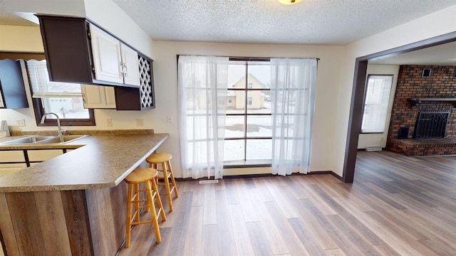 kitchen with sink, light hardwood / wood-style flooring, a textured ceiling, a fireplace, and a breakfast bar area