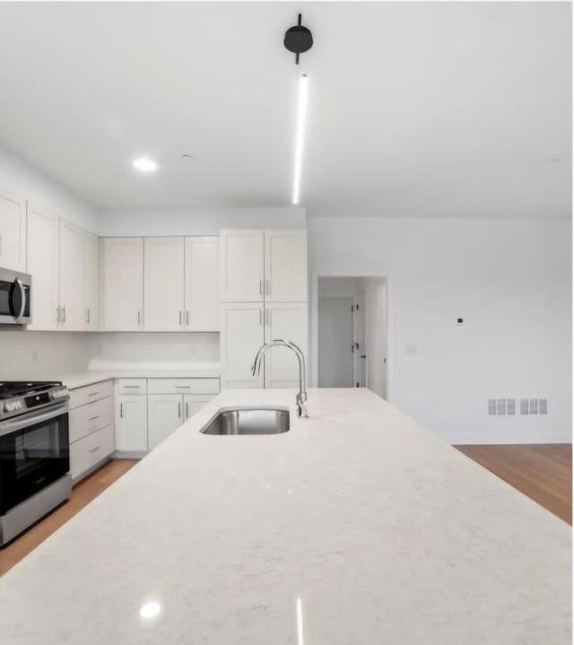 kitchen with sink, white cabinetry, light wood-type flooring, and appliances with stainless steel finishes