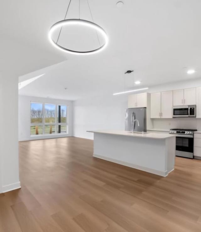 kitchen featuring white cabinets, light hardwood / wood-style flooring, hanging light fixtures, a center island with sink, and appliances with stainless steel finishes