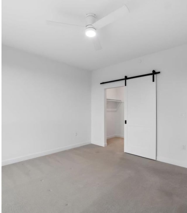 unfurnished bedroom featuring a closet, ceiling fan, carpet, and a barn door