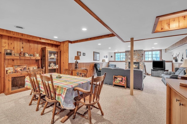 carpeted dining space with a stone fireplace and wooden walls