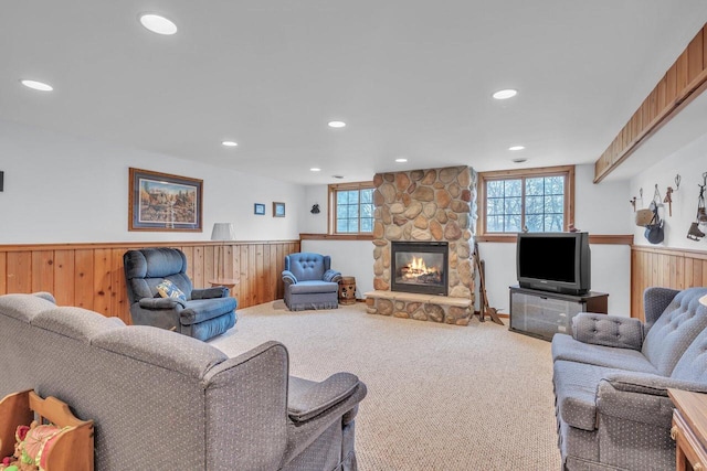 living room with carpet, a stone fireplace, and wood walls