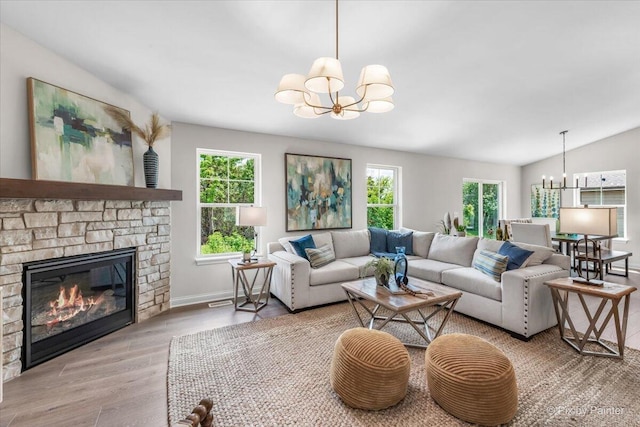 living room with lofted ceiling, light wood-type flooring, a stone fireplace, and a notable chandelier