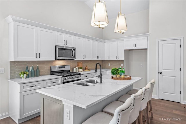 kitchen featuring sink, stainless steel appliances, decorative light fixtures, a center island with sink, and white cabinets