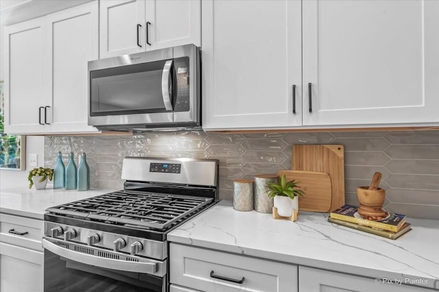 kitchen featuring decorative backsplash, light stone countertops, white cabinetry, and appliances with stainless steel finishes