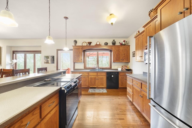 kitchen featuring sink, decorative light fixtures, light hardwood / wood-style flooring, and black appliances