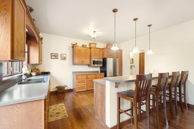 kitchen with pendant lighting, a breakfast bar, sink, dark hardwood / wood-style floors, and appliances with stainless steel finishes