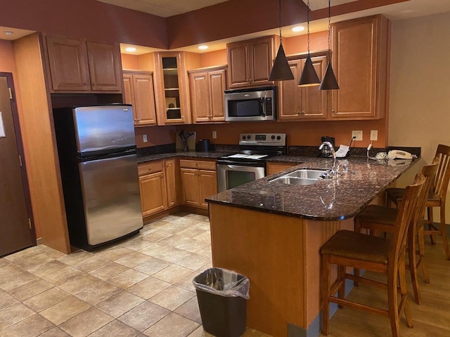 kitchen with kitchen peninsula, appliances with stainless steel finishes, dark stone counters, sink, and hanging light fixtures