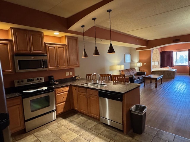 kitchen featuring kitchen peninsula, stainless steel appliances, sink, light hardwood / wood-style floors, and hanging light fixtures