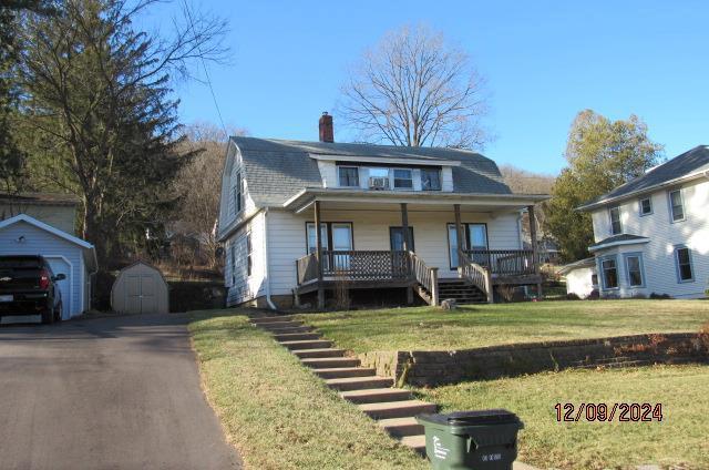 bungalow with covered porch, a garage, a storage unit, and a front yard