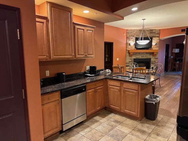 kitchen with dishwasher, a stone fireplace, sink, a textured ceiling, and light hardwood / wood-style floors