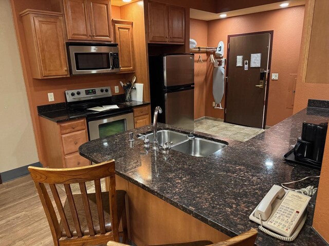 kitchen featuring dark stone countertops, sink, appliances with stainless steel finishes, and light hardwood / wood-style flooring