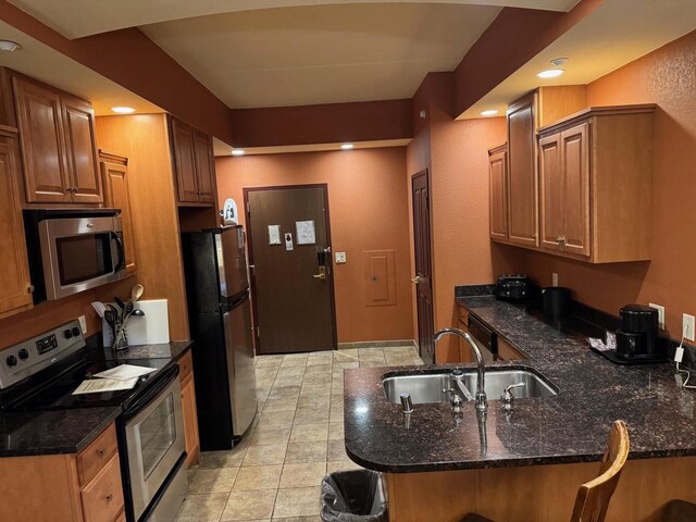 kitchen featuring kitchen peninsula, stainless steel appliances, dark stone countertops, and sink