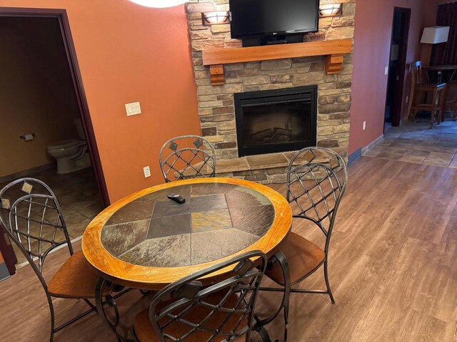 dining area with a stone fireplace and wood-type flooring