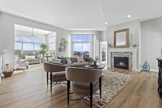 living room with a stone fireplace, ceiling fan, and light hardwood / wood-style flooring