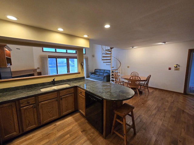 kitchen with kitchen peninsula, sink, dark stone countertops, hardwood / wood-style floors, and black dishwasher