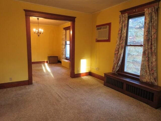 carpeted empty room with radiator heating unit, plenty of natural light, and an inviting chandelier