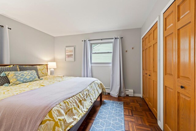 bedroom with dark parquet flooring, a baseboard heating unit, and multiple closets