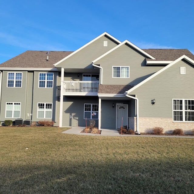 rear view of house featuring a balcony, central AC unit, and a lawn