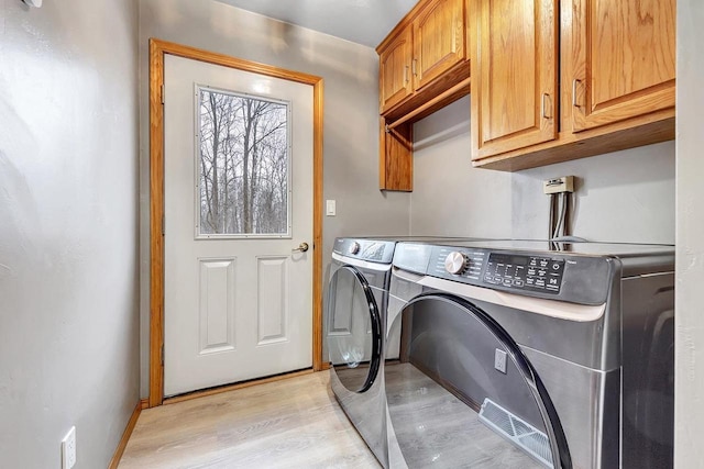 laundry area with cabinets, separate washer and dryer, and light hardwood / wood-style flooring