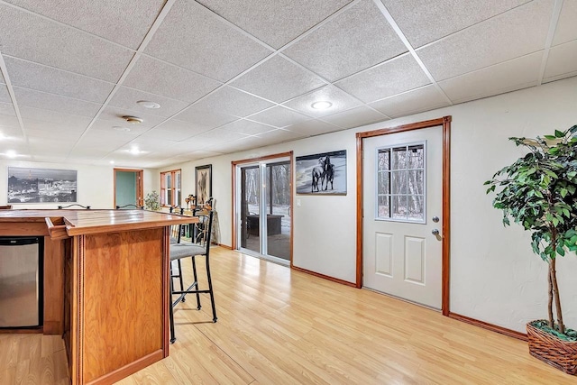 kitchen featuring a kitchen breakfast bar, stainless steel refrigerator, a paneled ceiling, and light hardwood / wood-style floors