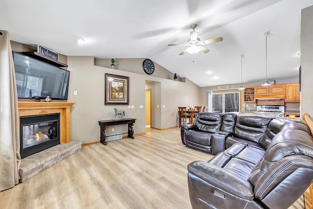 living room featuring sink, vaulted ceiling, ceiling fan, a fireplace, and light hardwood / wood-style floors