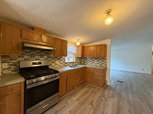 kitchen with light wood-type flooring, tasteful backsplash, stainless steel range, a textured ceiling, and sink