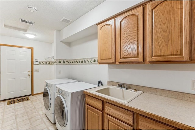 clothes washing area featuring a textured ceiling, cabinets, washing machine and clothes dryer, and sink