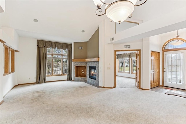 unfurnished living room with high vaulted ceiling, a premium fireplace, an inviting chandelier, and light colored carpet