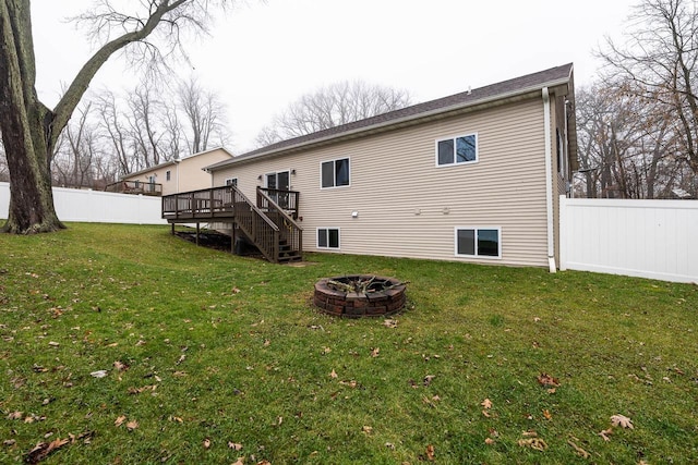 rear view of property featuring fence, a wooden deck, stairs, a fire pit, and a lawn