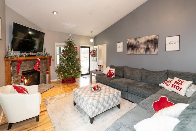 living area with a stone fireplace, lofted ceiling, and wood finished floors