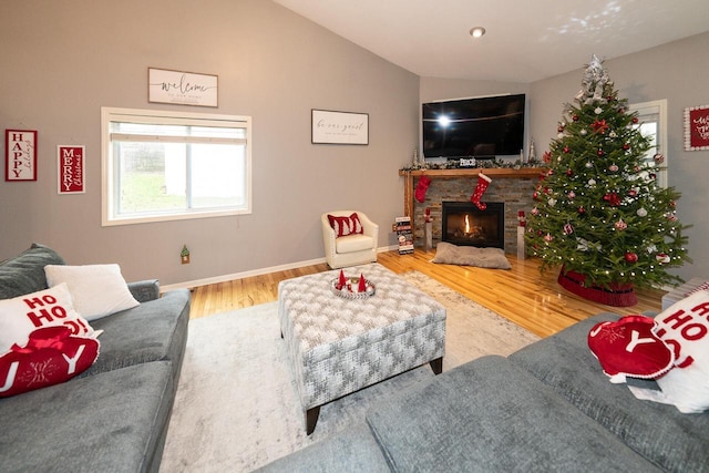 living area featuring baseboards, lofted ceiling, a stone fireplace, and wood finished floors