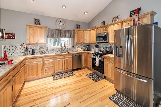 kitchen with light countertops, lofted ceiling, decorative backsplash, appliances with stainless steel finishes, and a sink