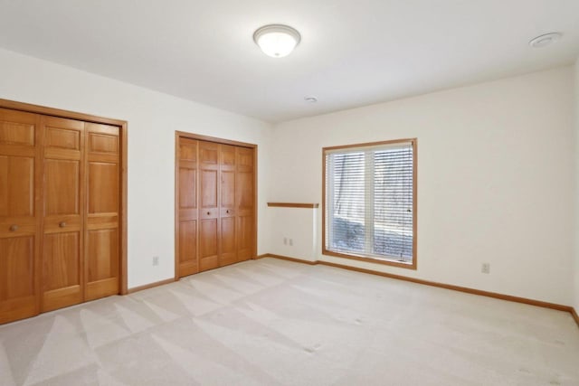 unfurnished bedroom with light colored carpet and two closets