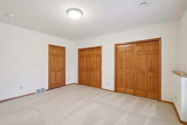 unfurnished bedroom featuring light carpet and two closets