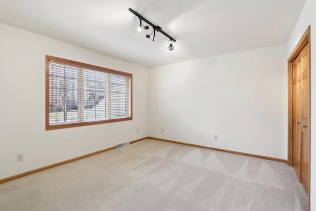 unfurnished bedroom featuring light colored carpet, rail lighting, and a closet