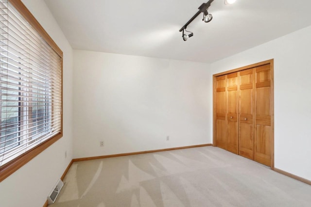 unfurnished bedroom featuring a closet, light colored carpet, and track lighting