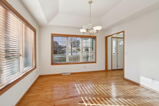 unfurnished dining area featuring a raised ceiling, light hardwood / wood-style floors, and an inviting chandelier