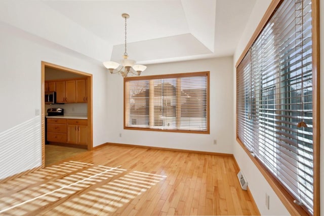 unfurnished dining area with a tray ceiling, light hardwood / wood-style flooring, and an inviting chandelier