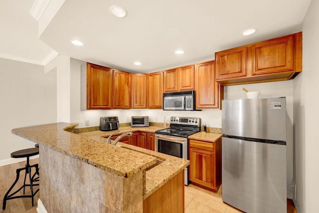 kitchen featuring kitchen peninsula, a kitchen breakfast bar, light stone countertops, stainless steel appliances, and crown molding