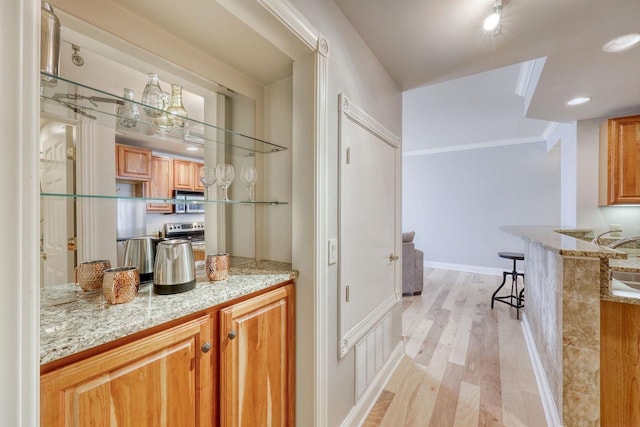 bar with light hardwood / wood-style floors, light stone counters, stainless steel range with electric stovetop, and crown molding