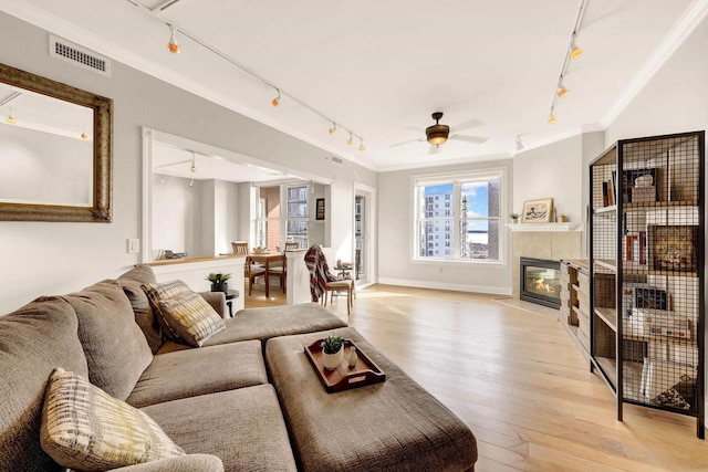 living room with ceiling fan, light wood-type flooring, crown molding, and a tile fireplace