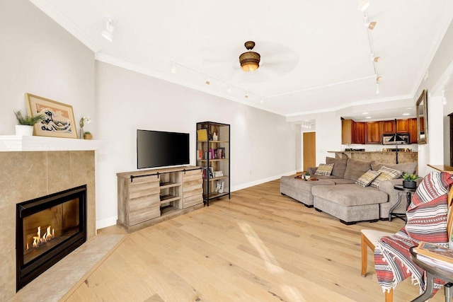 living room featuring crown molding, a fireplace, track lighting, and light wood-type flooring