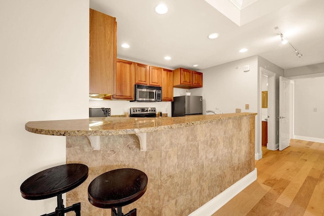 kitchen with a breakfast bar, appliances with stainless steel finishes, light wood-type flooring, and kitchen peninsula