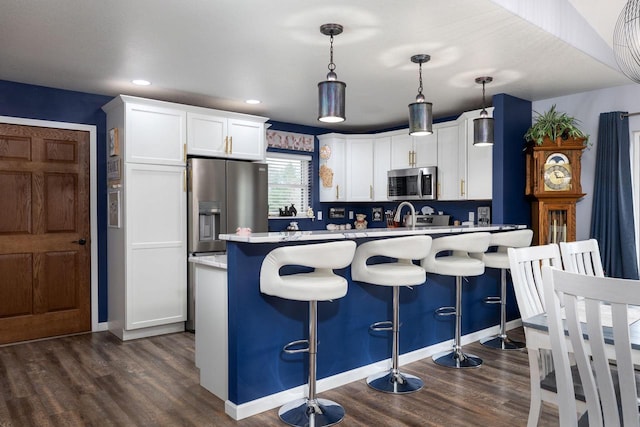 kitchen with stainless steel appliances, dark hardwood / wood-style floors, decorative light fixtures, a breakfast bar, and white cabinets