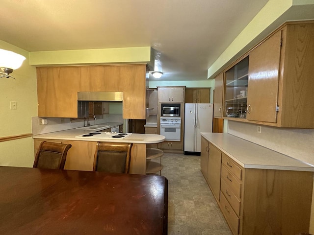 kitchen with a breakfast bar, sink, white appliances, and kitchen peninsula