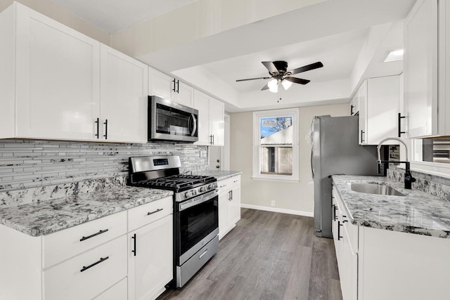 kitchen with light stone countertops, appliances with stainless steel finishes, sink, light hardwood / wood-style flooring, and white cabinets