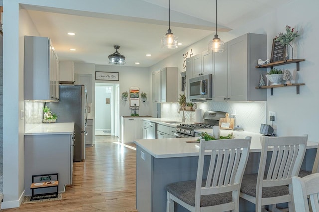 kitchen with hanging light fixtures, stainless steel appliances, backsplash, kitchen peninsula, and light wood-type flooring