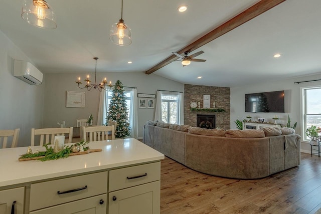 living room featuring light hardwood / wood-style flooring, lofted ceiling with beams, an AC wall unit, a fireplace, and ceiling fan with notable chandelier