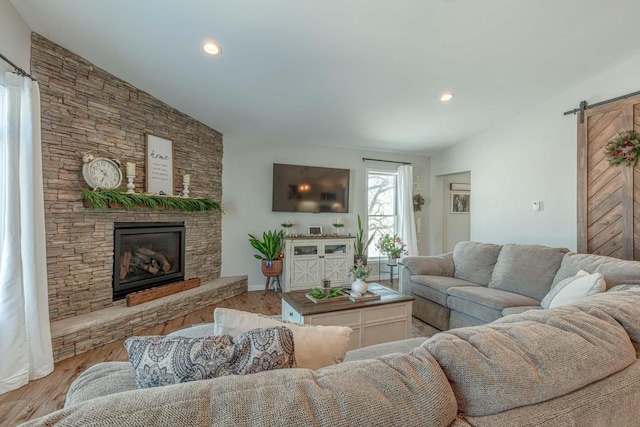 living room with a stone fireplace, light hardwood / wood-style floors, lofted ceiling, and a barn door